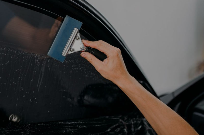 Professional applying tint film to the windows of a car for enhanced privacy and UV protection.